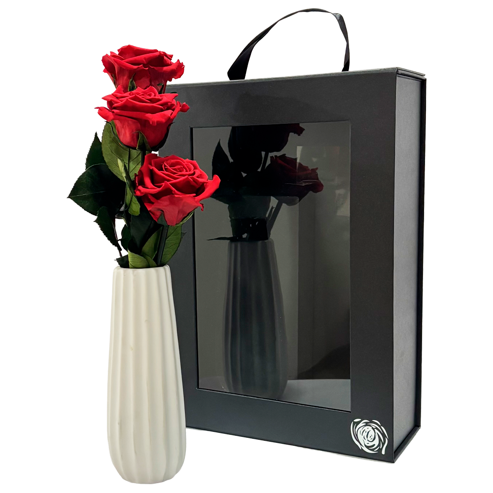 Black gift box with a clear front window, beside a white vase holding red roses.